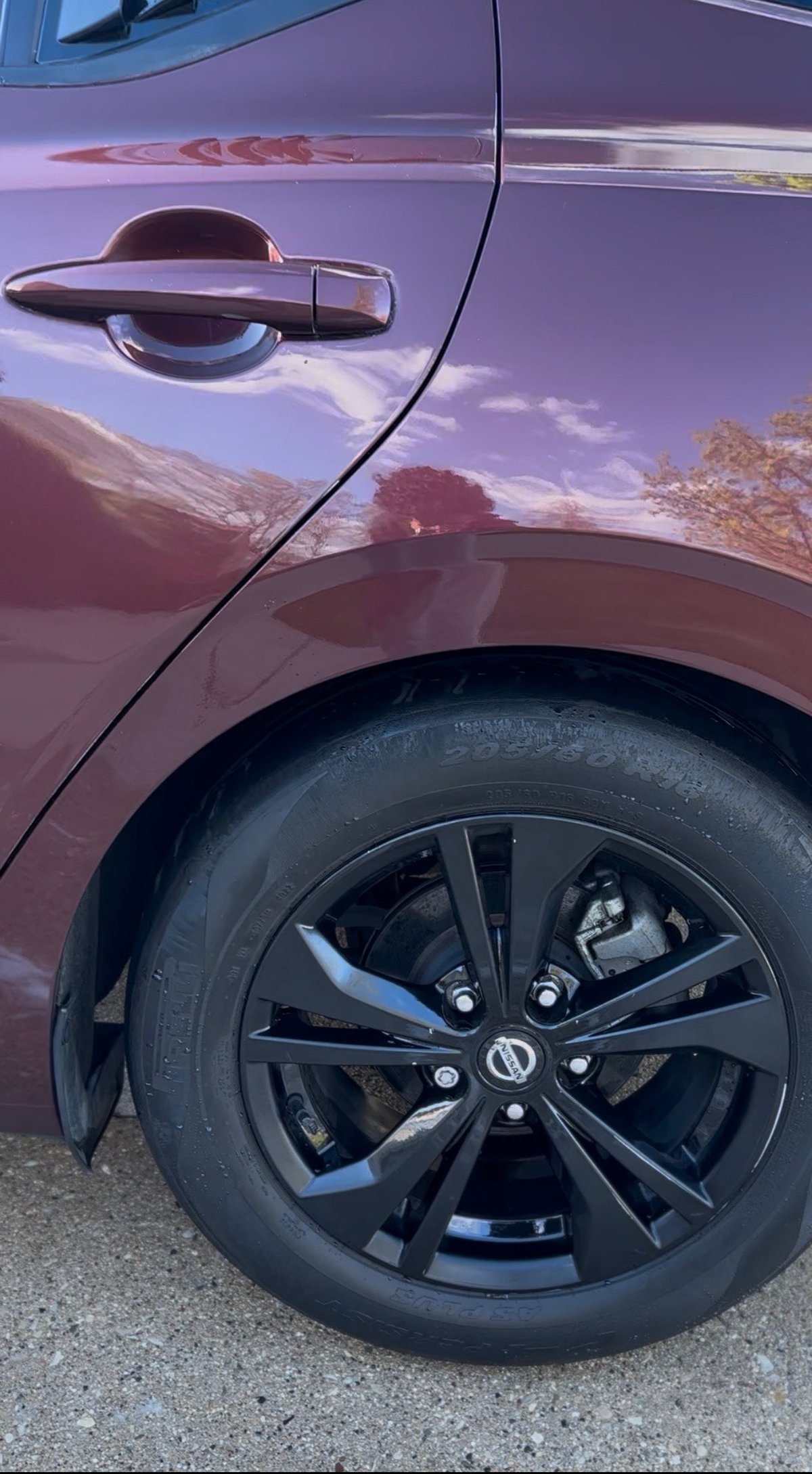 Close-up of purple cars side door handle, wheel, and tire with scenic landscape reflection in body panel