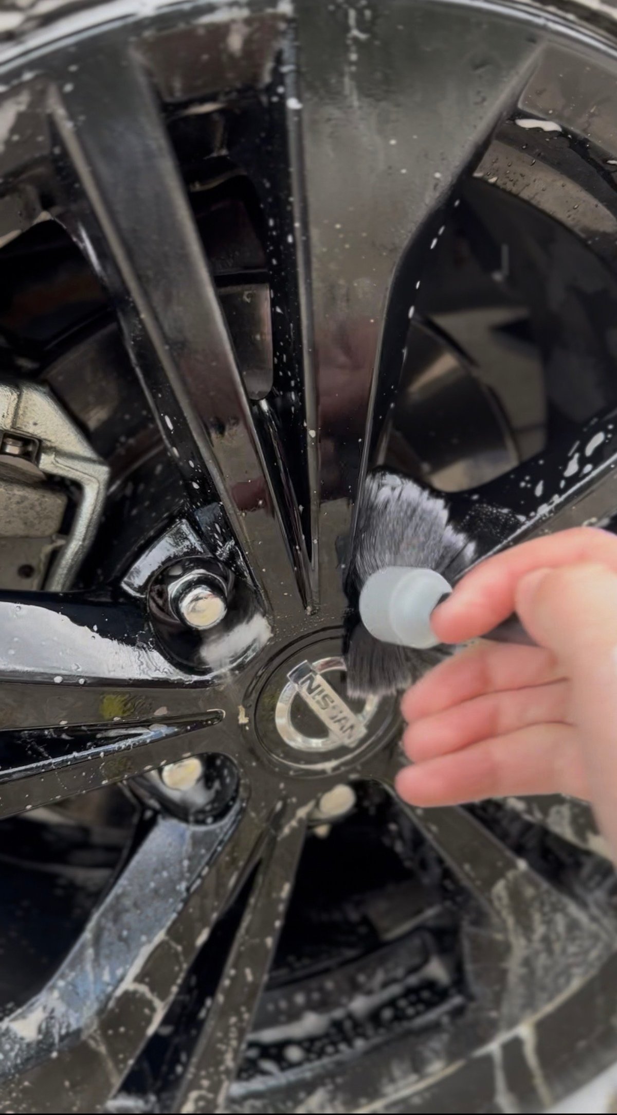 Hand cleaning a wet black car wheel with a brush during car wash