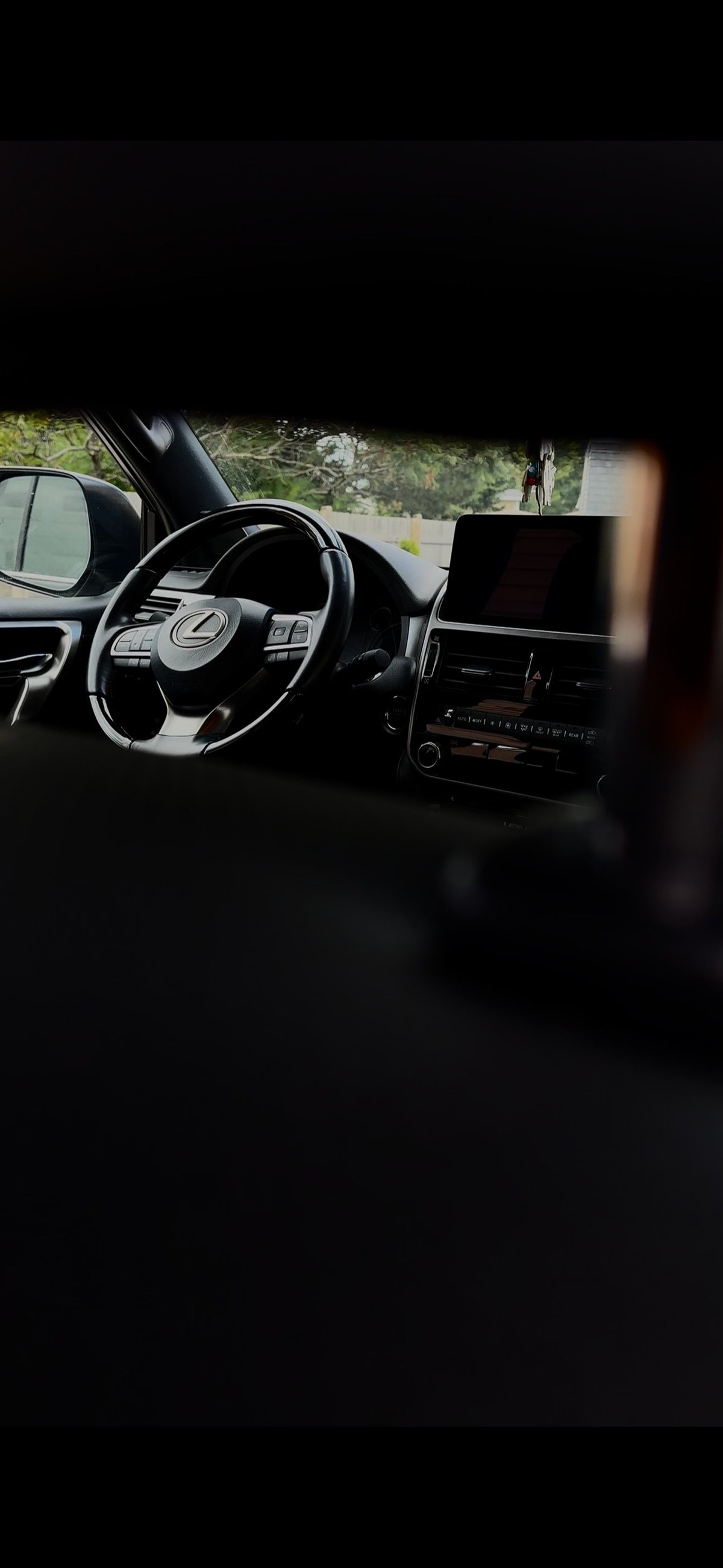 Car interior shot from passenger seat showing steering wheel, dashboard with touchscreen, and view of parking lot through windshield