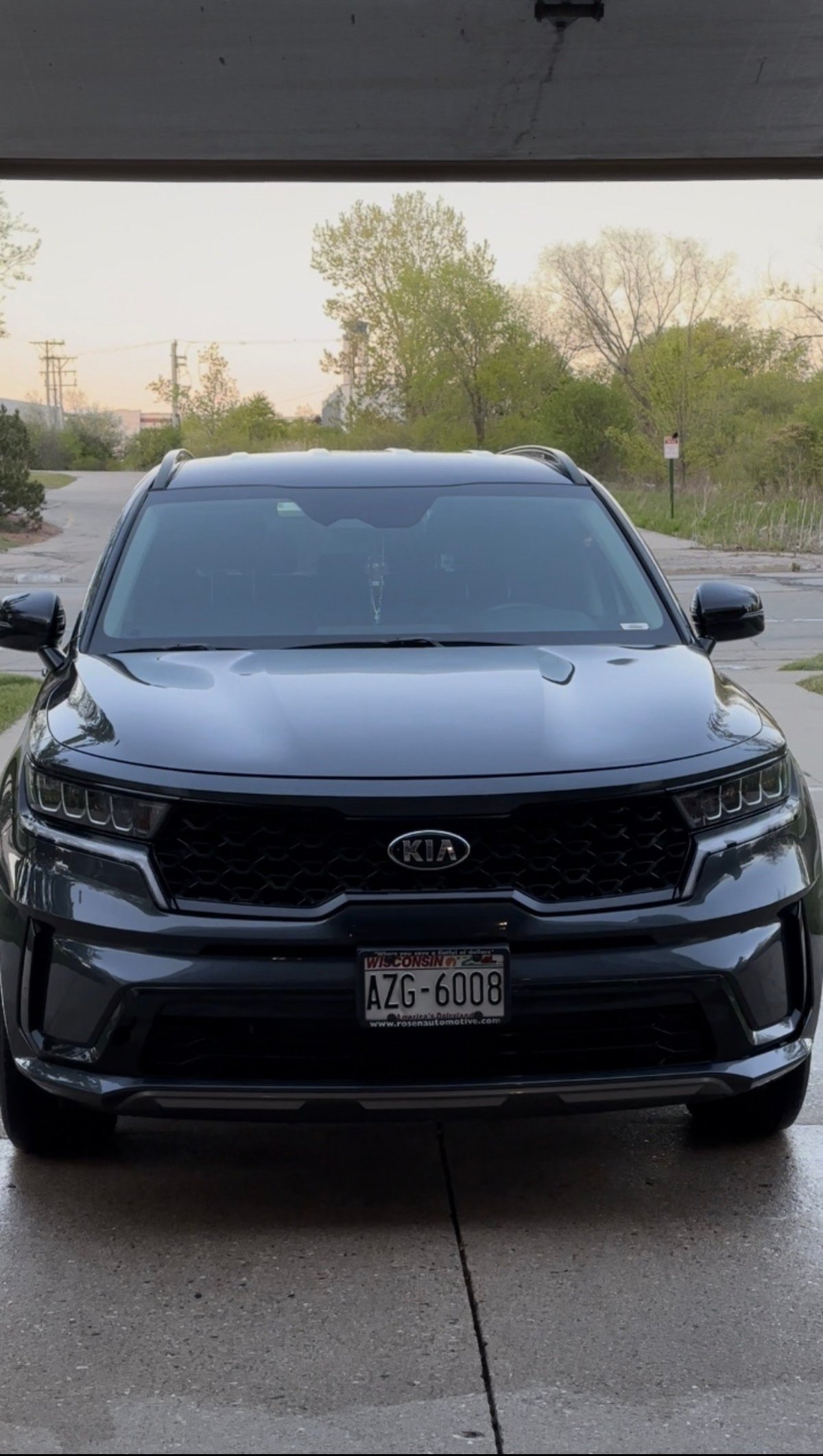 Black Kia SUV parked on wet pavement with spring trees in background, front view showing license plate and LED headlights
