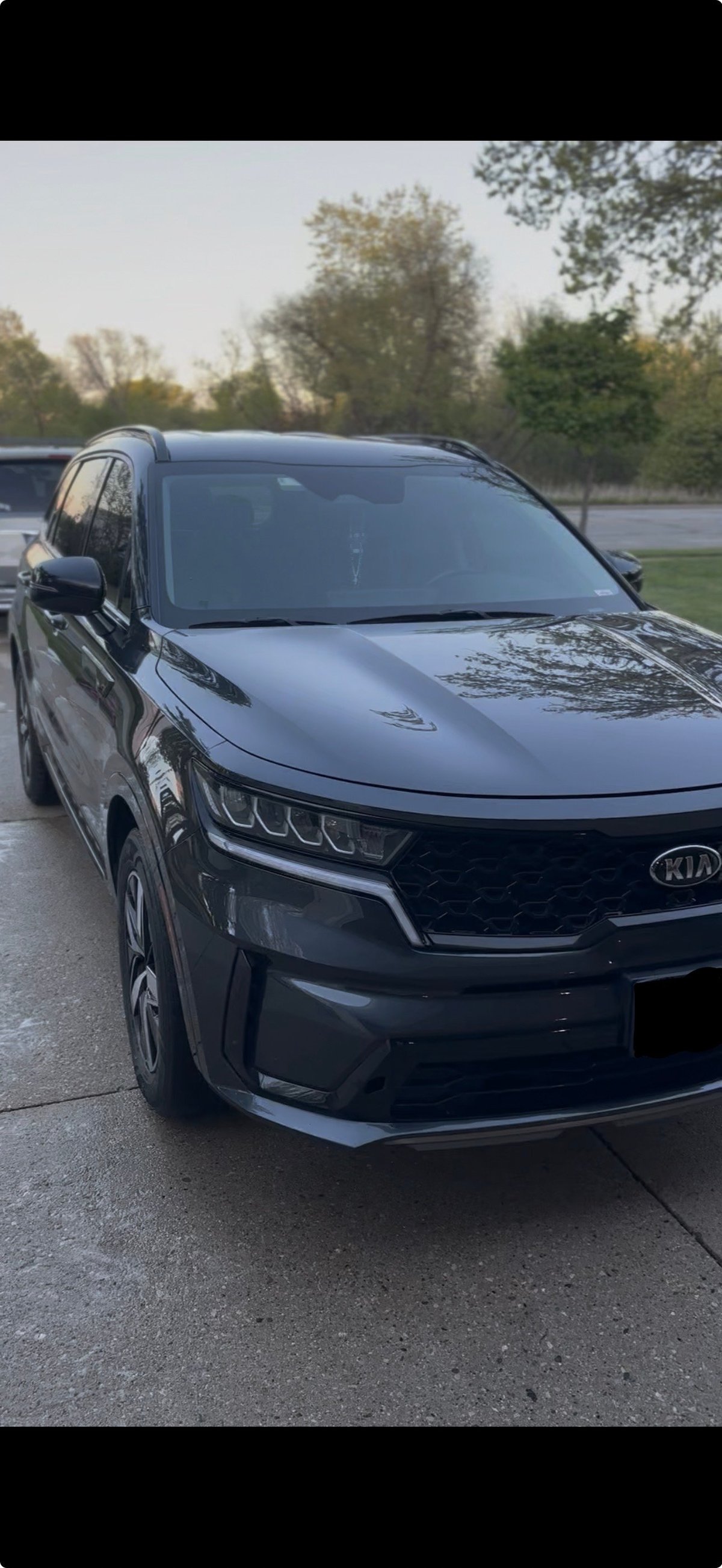 Black Kia SUV parked on a wet pavement with trees in the background during daytime