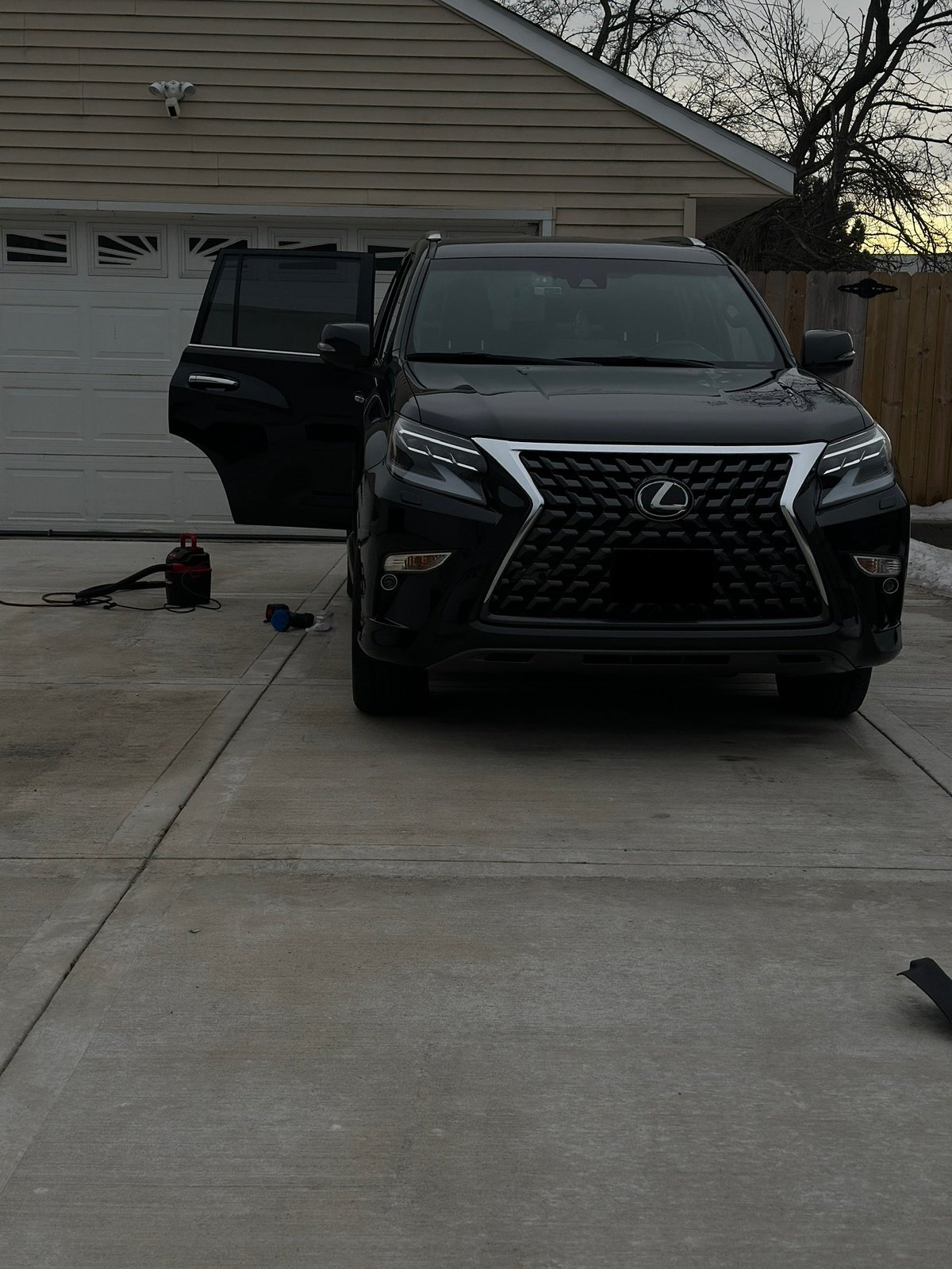 Black Lexus SUV parked in driveway with open drivers door, garage in background