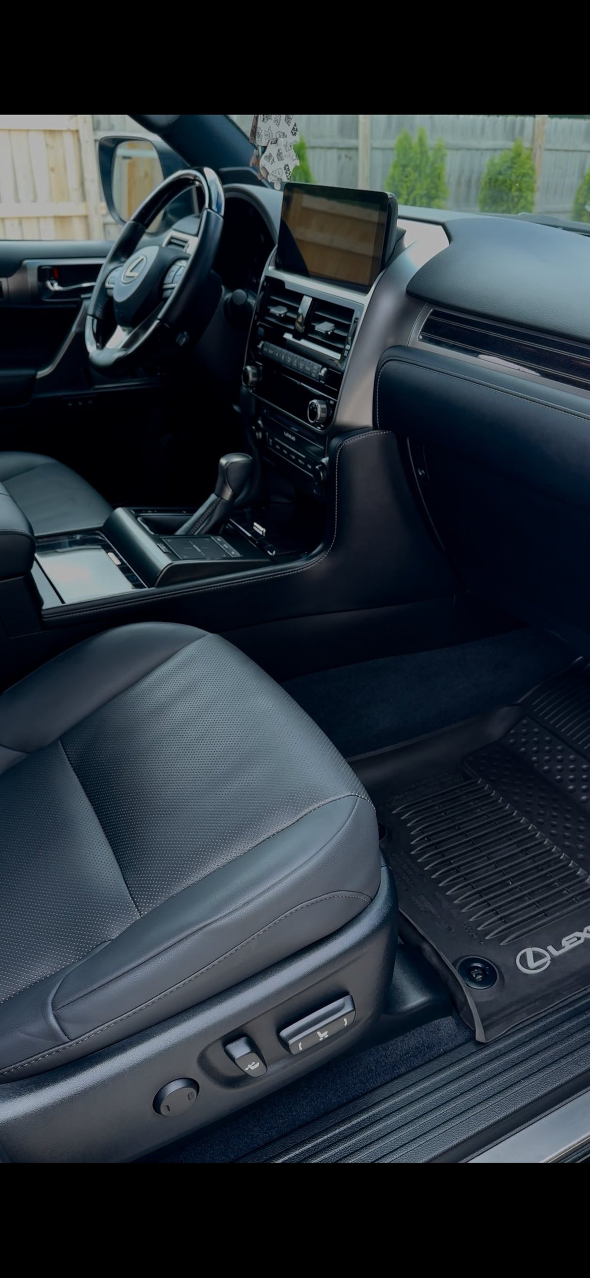 Luxury car interior showing leather seats, steering wheel, touchscreen display, and dashboard with suburban background visible through windshield